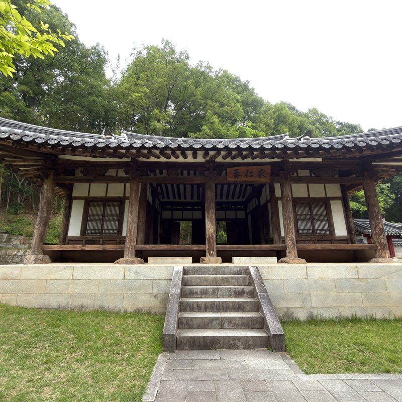 여름 숲 앞, 돌계단 위에 선 경내의 한옥 한 채.